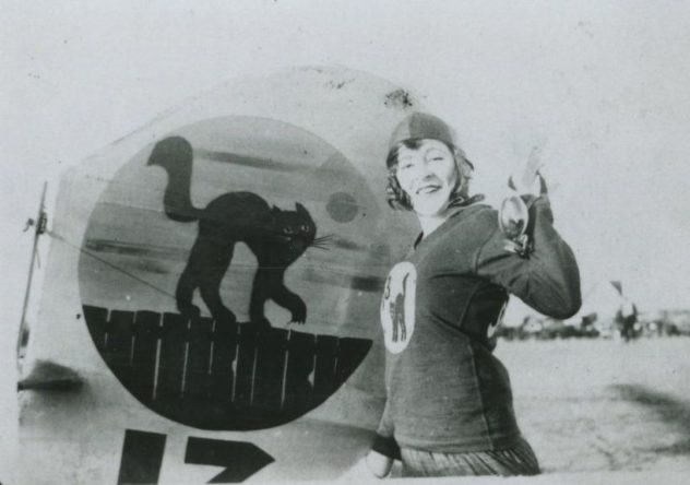 Image of Gladys Roy from the 13 Flying Black Cats, standing beside the logo on the tail of their aircraft