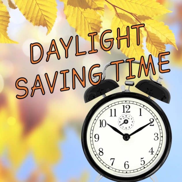 fall skyline behind a black alarm clock with Daylight Saving Time text overlaid